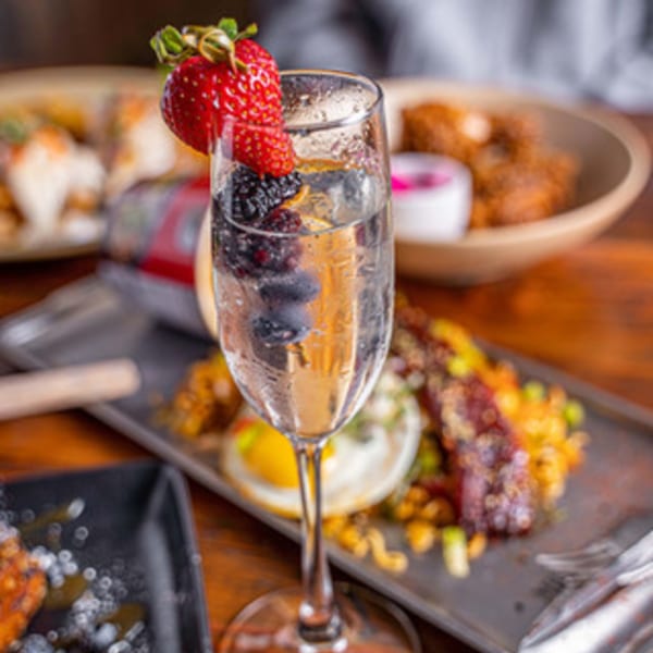 A champagne flute with berries and a strawberry garnish, with Korean food in the background.