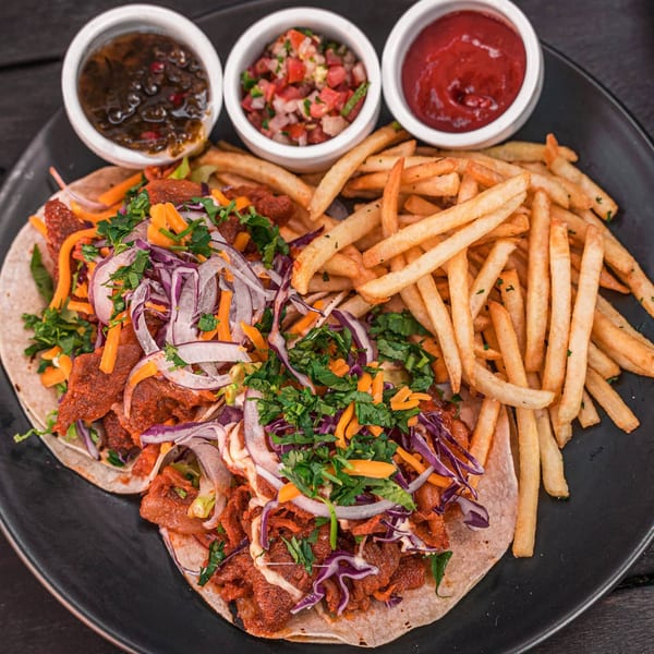 Two Korean tacos with fries and three dipping sauces on a black plate.
