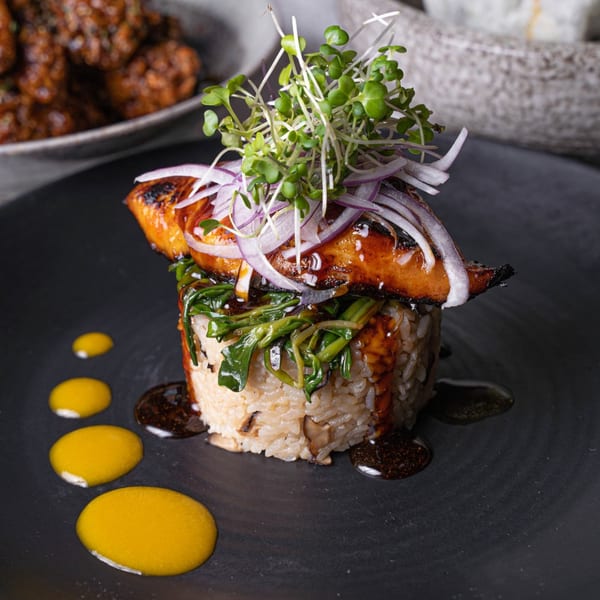 Surisan's Korean dish with glazed fish, rice, greens, red onions, and sprouts on a dark plate.