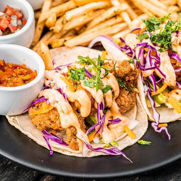 Two Surisan Korean fried chicken tacos with purple cabbage, sauce, and cilantro, served with fries and salsa.
