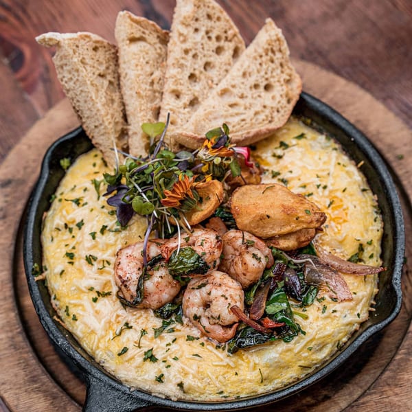 Surisan's Korean-style cheesy egg souffle with shrimp, fried potatoes, and microgreens in a skillet.