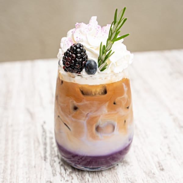 A Surisan Korean latte with purple syrup, ice, cream, blackberry, blueberry, and rosemary.