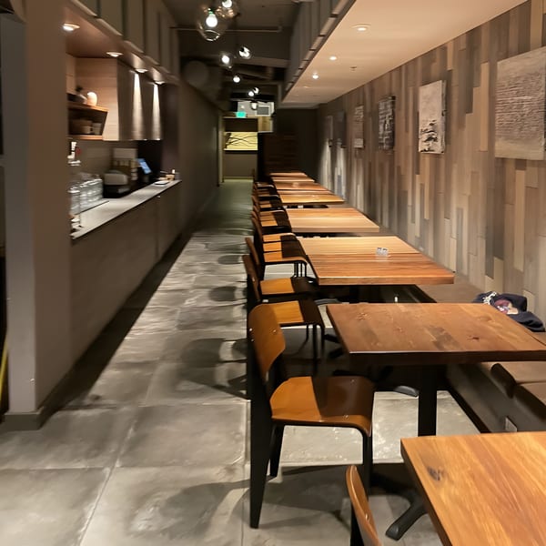 Long, narrow dining room at Surisan with wooden tables and chairs, a counter, and textured wall art.