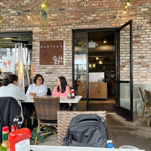 Three women seated at an outdoor table on the patio of Surisan, a Korean restaurant.