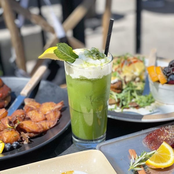 A vibrant green drink with whipped cream, mint, and lemon, surrounded by various Korean dishes.