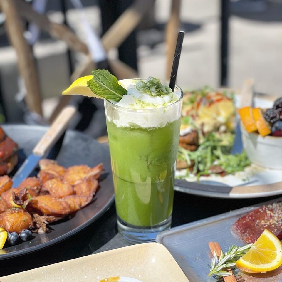 A vibrant green drink with whipped cream, mint, and lemon, surrounded by various Korean dishes.