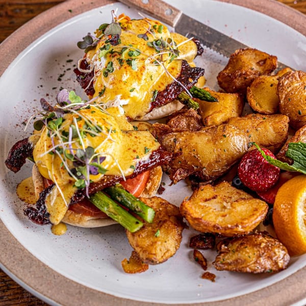 Surisan's Eggs Benedict with bacon, asparagus, and tomatoes, served with roasted potatoes and fruit.
