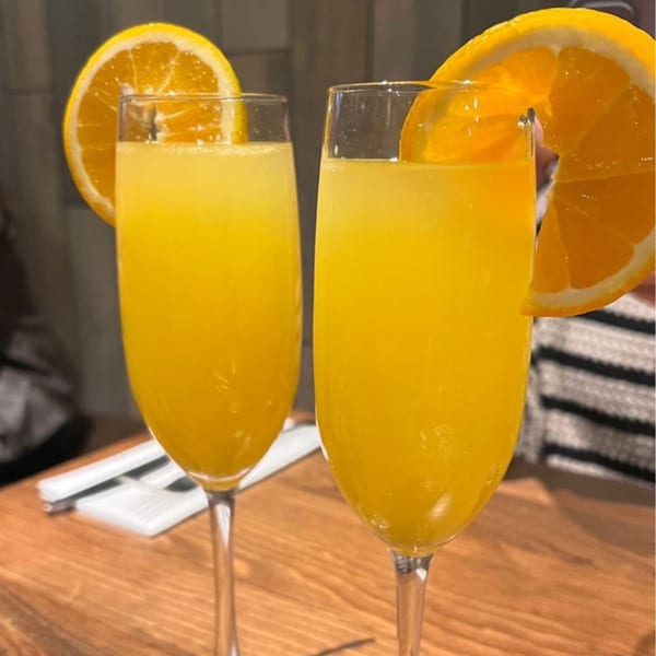 Two mimosa cocktails garnished with orange slices on a wooden table at Surisan.