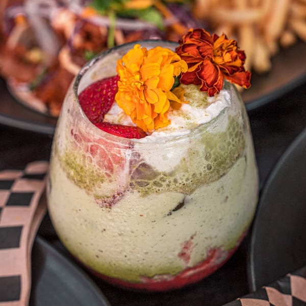 A Surisan dessert drink with green layers, strawberries, whipped cream, and orange flowers.