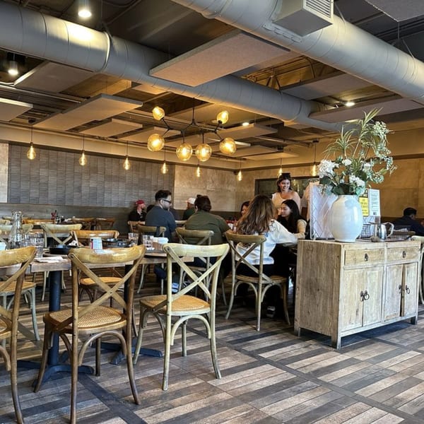 Diners seated at wooden tables in the Surisan restaurant, with exposed ductwork and modern lighting.
