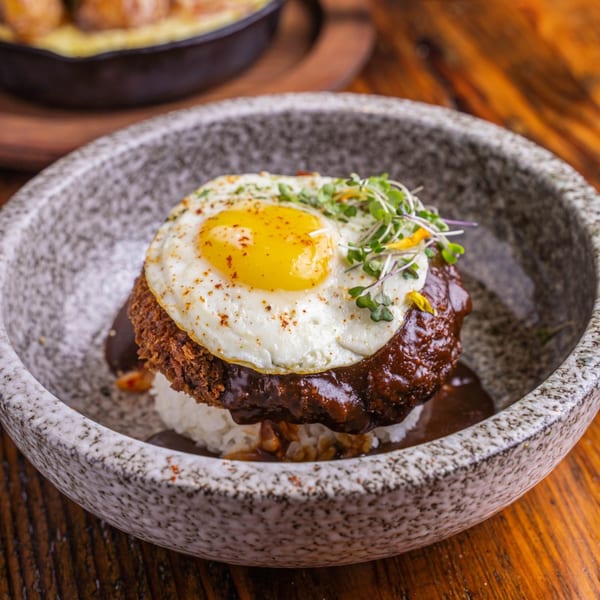 Surisan's Loco Moco with a fried egg, gravy, and microgreens in a speckled bowl.