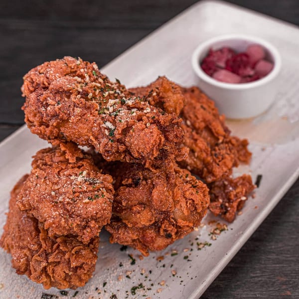 Crispy Korean fried chicken pieces, sprinkled with seasoning, served on a white plate with pickled radishes.