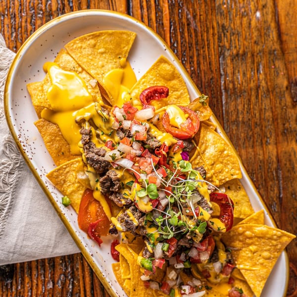 Surisan's Korean nachos with bulgogi, melted cheese, pico de gallo, and microgreens on a white platter.