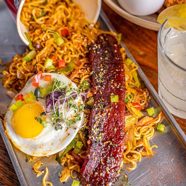 Surisan's spicy Korean ramen with a fried egg, pork belly, and vegetables on a metal tray.