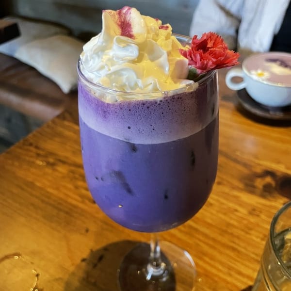 Purple Surisan ube drink with whipped cream and a red flower on a wooden table.