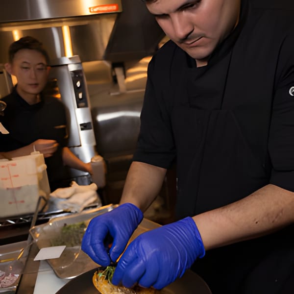 A chef in blue gloves meticulously garnishes a dish in a bustling Korean restaurant kitchen.